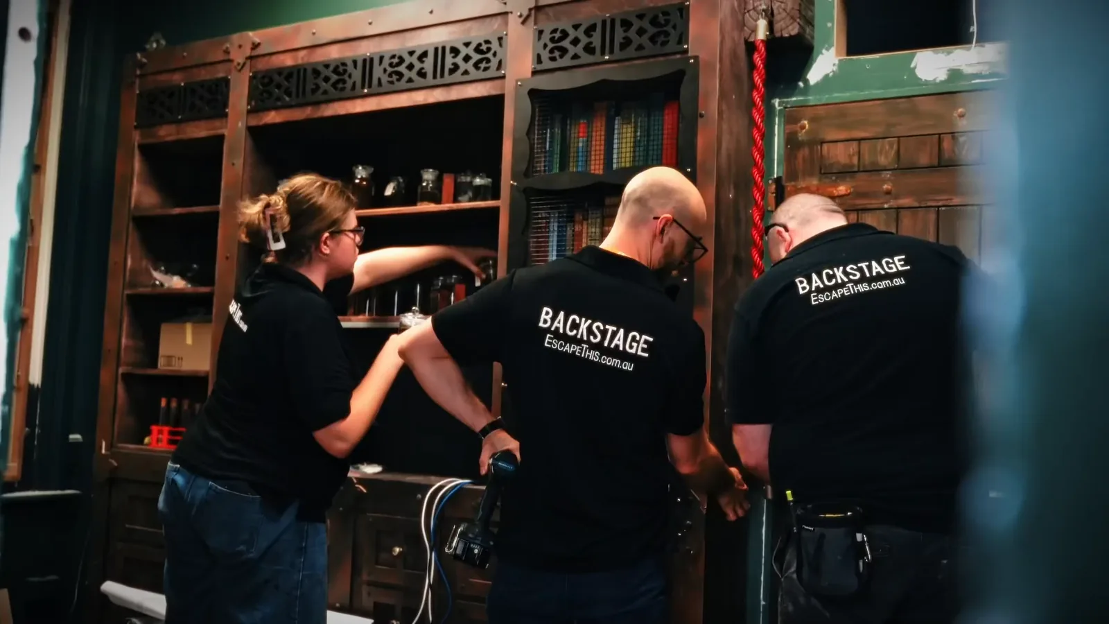 Escape This set builders dressing a library bookcase set during an escape room install